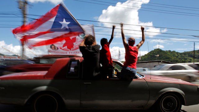 People ride atop a vehicle waving a Puerto Rican flag during elections in San Juan, Puerto Rico, Tuesday, Nov. 6, 2012. Puerto Ricans are electing a governor as the U.S. island territory does not get a vote in the U.S. presidential election.
