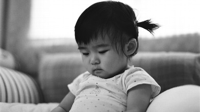 PHOTO: Baby with braids sitting on bed looking down