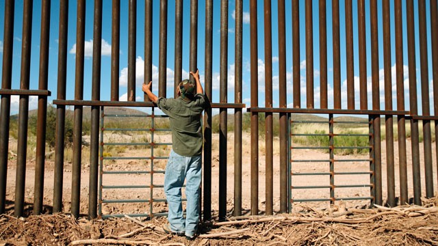 PHOTO:&nbsp;A man stands at a border fence between the United States and Mexico.