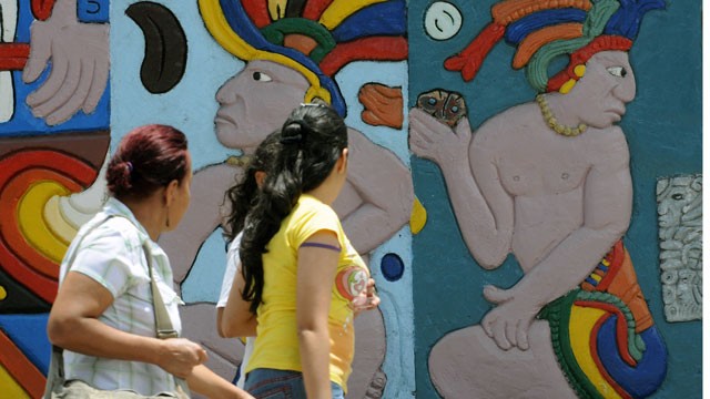 PHOTO: Women walk by a wall displaying Maya figures.