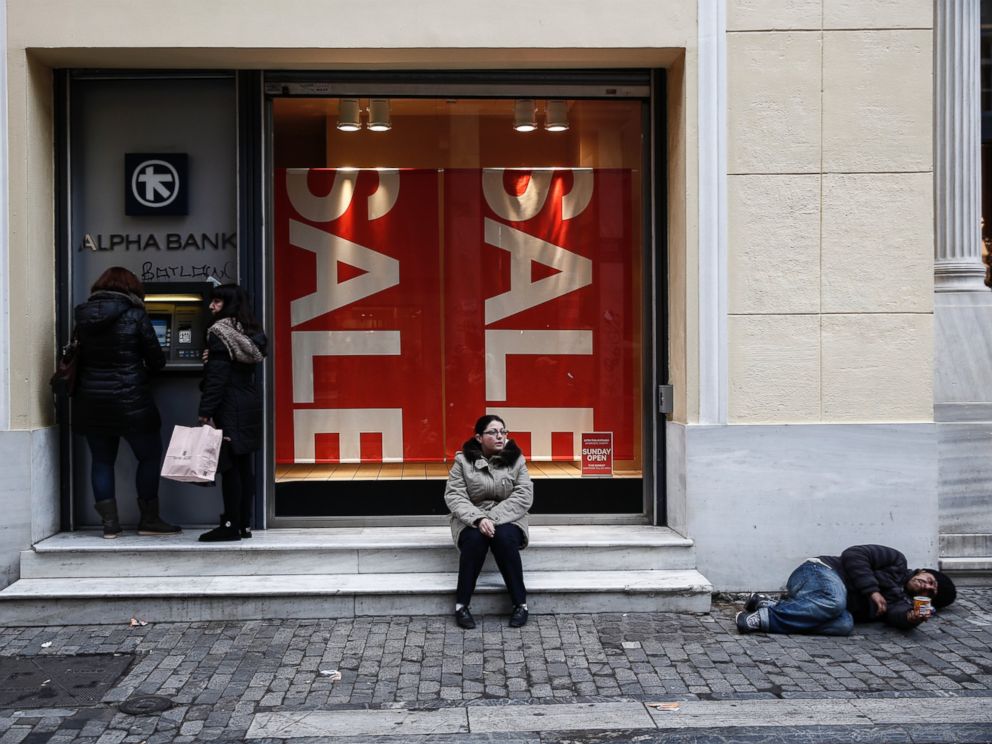 PHOTO: Women make a transaction at an ATM as a man begs on Ermou Street, Athens main shopping strip