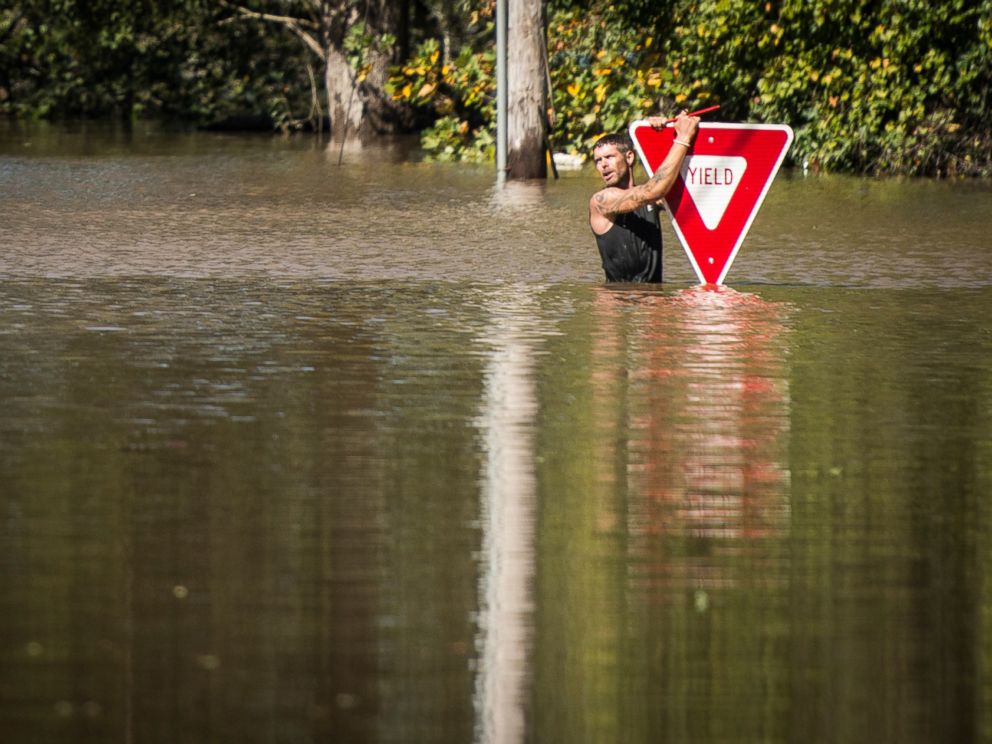 PHOTO: A man holds onto a yield sign after trying to swim out to help a stranded truck driver at NC 301 Highway and Tom Starling Road in Hope Mills, North Carolina, on Oct. 9, 2016. 