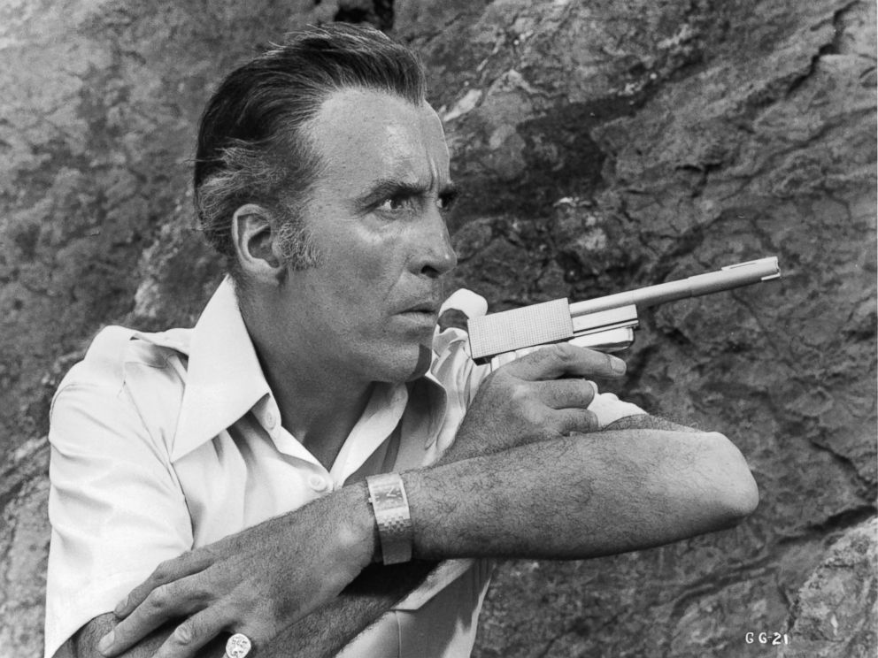 PHOTO: Christopher Lee along side a cliff wall pointing a gun in a scene from the film The Man With The Golden Gun, 1974.
