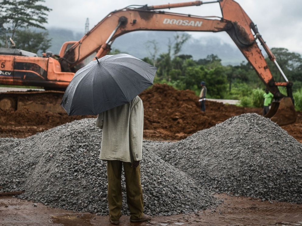 PHOTO: A man with an umbrella watches workers from the International Committee of the Red Cross during the construction a brand new health center in Kenema, Sierra Leone on Aug. 25, 2014.