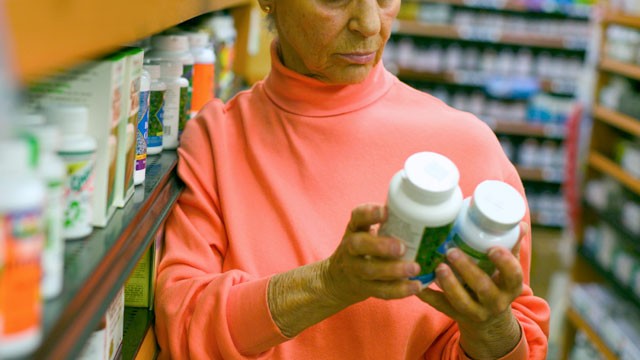 PHOTO: A woman compares vitamins in a pharmacy.