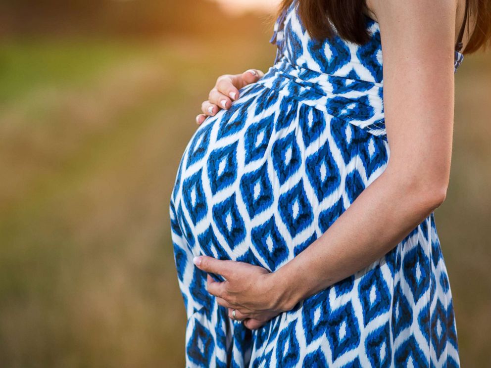 PHOTO: A pregnant woman poses in blue dress cradling her belly in this stock image.
