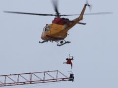 PHOTO: A rescue worker is lowered from a military helicopter as they retrieve a crane operator