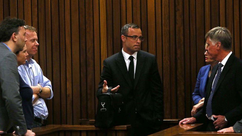 PHOTO: Oscar Pistorius, speaks with family and friends at right as press look on, March 25, 2014 in Pretoria, South Africa.