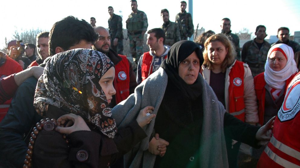 PHOTO: Syrian army soldiers look on as women walk towards a bus to evacuate the battleground city of Homs, Syria, Feb. 9, 2014.