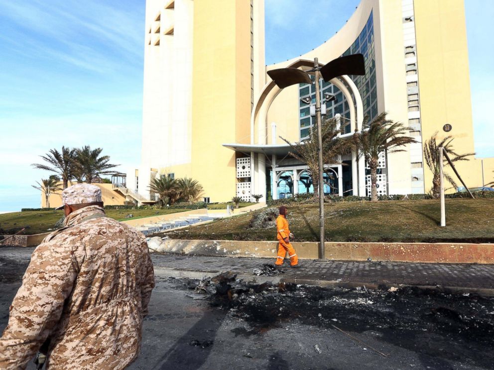 PHOTO: A member of security, left, for Tripolis central Corinthia Hotel looks on as sanitation workers clean the debris outside the hotel on Jan. 28, 2014.