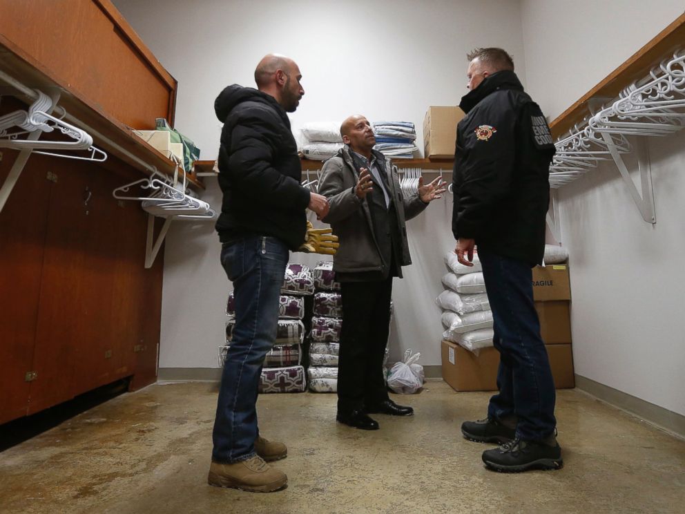 PHOTO: Fadel Alshawwa and Jean Pierre Venegas talk with Bill Spanjer, Municipal Emergency Coordinator for Emerson-Franklin, talk as they bring blankets and pillows into a community hall for refugees that may walk across the border in Emerson, Manitoba.