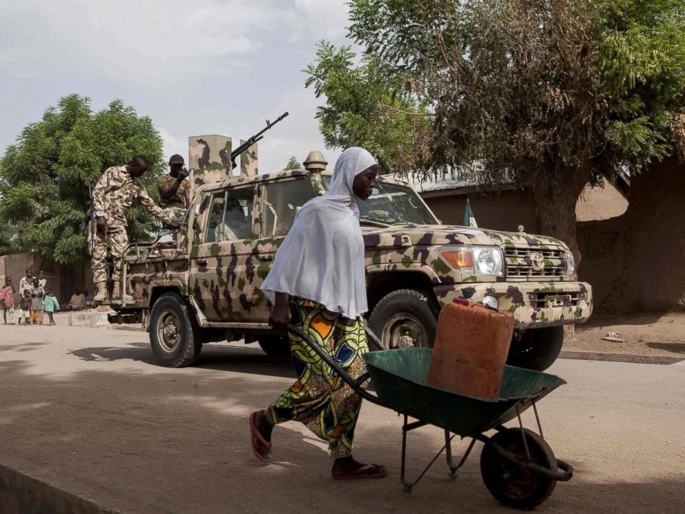 PHOTO: A woman pushes a wheelbarrow carrying a jerrycan filled with water as Nigerian soldiers patrol in the town of Banki in northeastern Nigeria, April 26, 2017.
