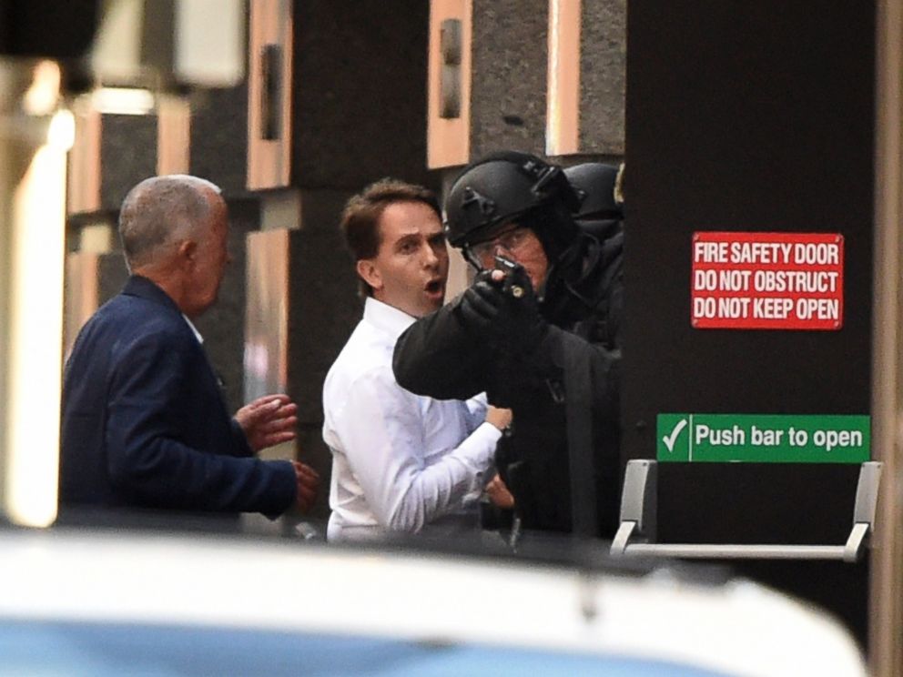 PHOTO: Two hostages, left, run for cover behind a policeman, right, during a hostage siege in the central business district of Sydney on Dec. 15, 2014. 