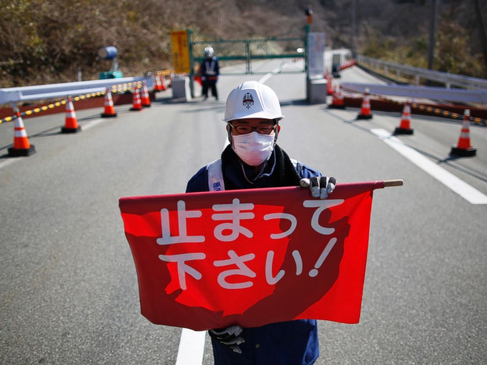 PHOTO: A security guard holds a flag, which reads Please Stop!, as he stand by a steel gate at the border near Fukushima