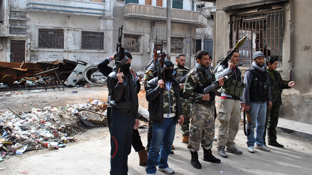 PHOTO: Syrian rebels gather in front of the remains of a burnt military vehicle belonging to Syrian government forces destroyed by the rebels during clashes at Khaldiyeh neighborhood in Homs province, Syria on Feb. 23, 2012.