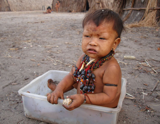 A female toddler, wearing traditional jewelry and eating yucca bread.