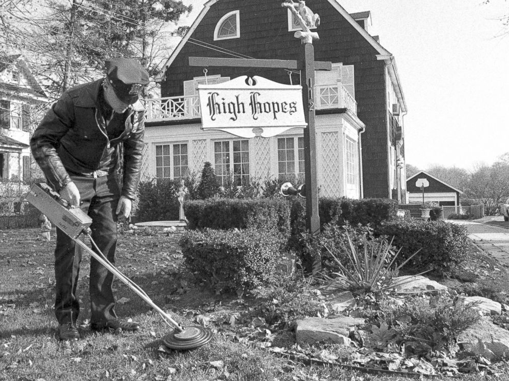 PHOTO: Suffolk County policeman uses mine detector as he sweeps through dead leaves on lawn of Ronald DeFeos 12-room, $75,000 Dutch colonial home in Amityville.