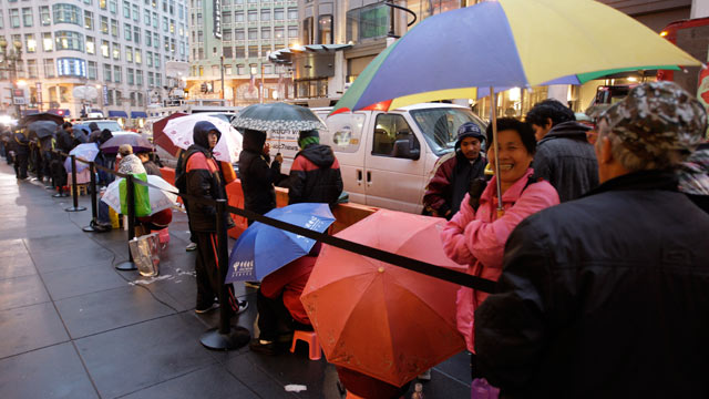 PHOTO: Apple customers take cover from the rain as they wait in line at an Apple store on the first day of the launch of the new iPad, in San Francisco, March 16, 2012.