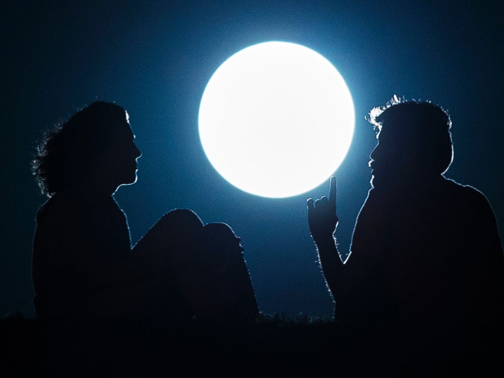 PHOTO: A couple talk as they sit against the perigee moon, also known as a supermoon, in Madrid, Aug. 10, 2014.