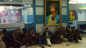PHOTO: A crowd sits under a photo of Col. Moammar Gadhafi in the airport in Tripoli.