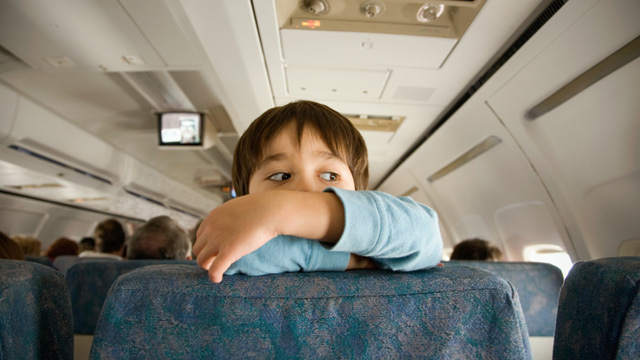 PHOTO: Child climbing and looking over back of airplane seat