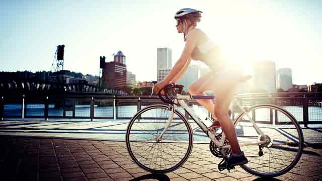 PHOTO: A woman commutes to work by bike, the evening sun setting over downtown Portland, Oregon and the Willamette River.