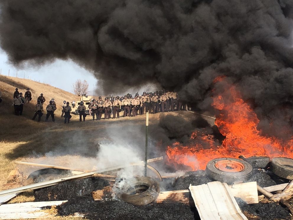 PHOTO: Tires burn as armed soldiers and law enforcement officers stand in formation on Oct. 27, 2016, to force Dakota Access pipeline protesters off private land where they had camped to block construction.