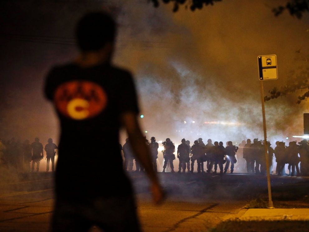 PHOTO: A man watches as police walk through a cloud of smoke during a clash with protesters, Aug. 13, 2014, in Ferguson, Mo.