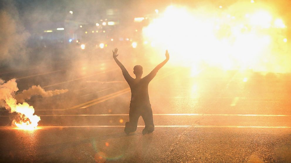 PHOTO: Tear gas surrounds a woman kneeling in the street with her hands in the air after a protest Aug. 17, 2014, in Ferguson, Mo.