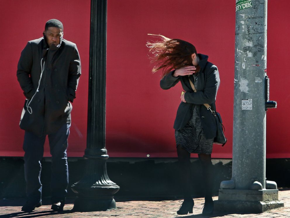 PHOTO: Three pedestrians waiting to cross the street in Boston are bundled up against the cold while being buffeted by high winds on March 18, 2015.