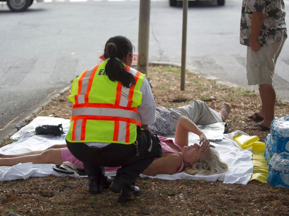 A paramedic checks on a woman, lying on a median, after she and others exited the Marco Polo apartment complex as firefighters continue to battle a blaze at the high-rise, Friday, July 14, 2017, in Honolulu. (AP Photo/Marco Garcia)