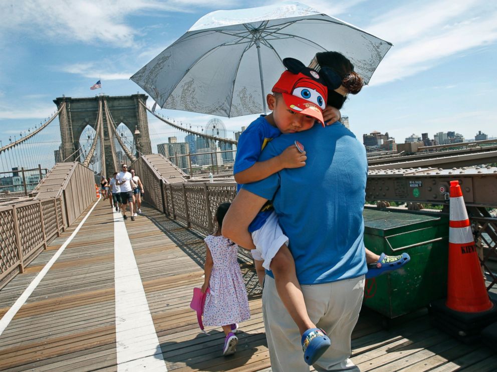 PHOTO: In this July 24, 2016, file photo, Xiuquin Huang carries her grandson Ruize Yan beneath an umbrella as she walks across the Brooklyn Bridge with her daughter and granddaughter Rina Wu.
