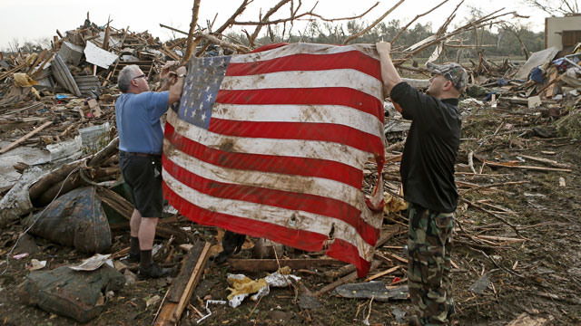 PHOTO: Clark Gardner, at left, and another man place an American flag on debris in a neighborhood off of Telephone Road in Moore, Okla., after a tornado moved through the area on Monday, May 20, 2013.