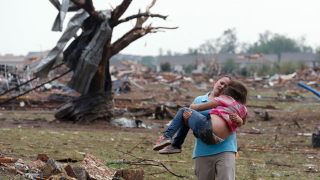 PHOTO: A woman carries her child through a field near the collapsed Plaza Towers Elementary School in Moore, Okla., May 20, 2013.