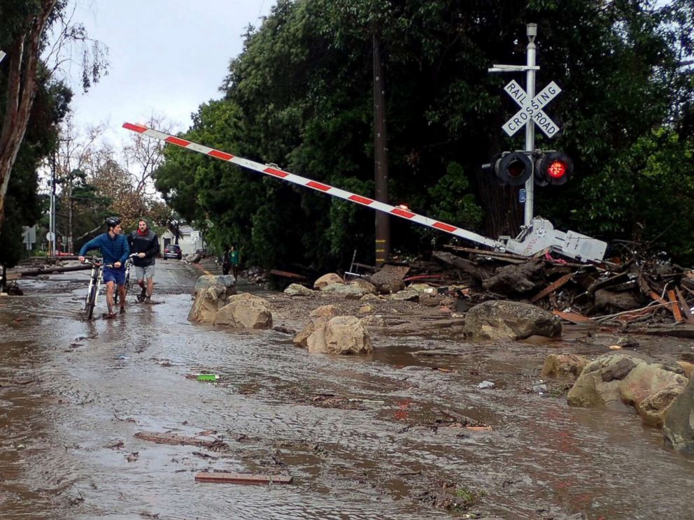 PHOTO: People walk through a crossing for the main line of the Union Pacific Railroad blocked with debris from mudslides following heavy rains in Montecito, California, January 9, 2018. 