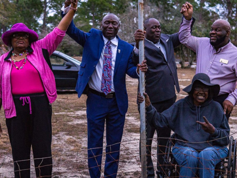 PHOTO: From left, Priscilla Davis, Ben Crump, Mayor Rufus Davis, Gwen Lillian Thomas, and Councilman Venterra Pollard hold hands in victory at a small portion of the fence left to be removed at Oakview Cemetery in Camilla, Ga., Jan. 11, 2018.