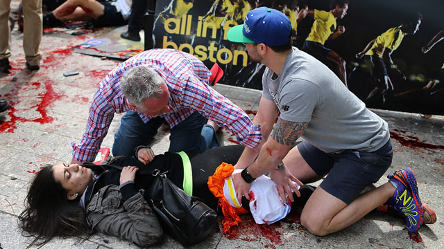 PHOTO: Bystanders help an injured woman at the scene of the first explosion on Boylston Street near the finish line of the 117th Boston Marathon.