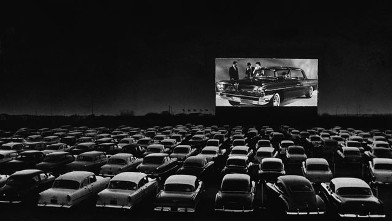PHOTO: Vehicles fill a drive-in theater while people on the screen stand near a new car, 1950s.