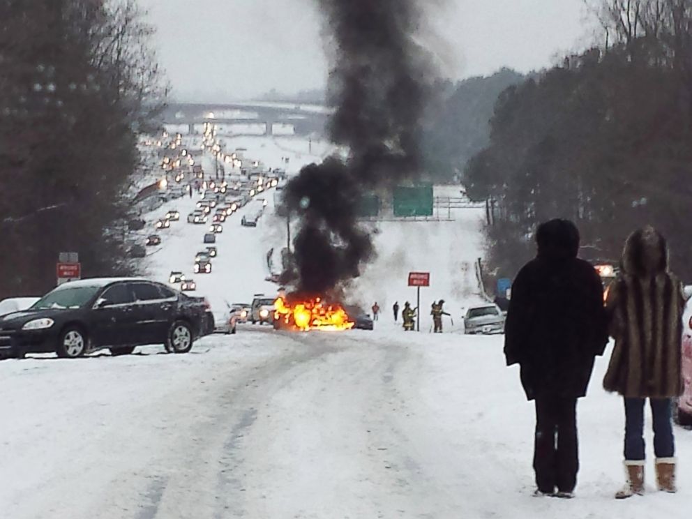 PHOTO: Motorists watch a vehicle burn after it caught fire while struggling to get up a snow covered hill in Raleigh, North Carolina on February 12, 2014.