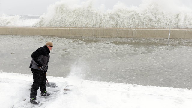 PHOTO: Mike Streeter shovels snow in his front yard as ocean water crashes over the sea wall just feet away on February 9, 2013 in Winthrop, Mass.