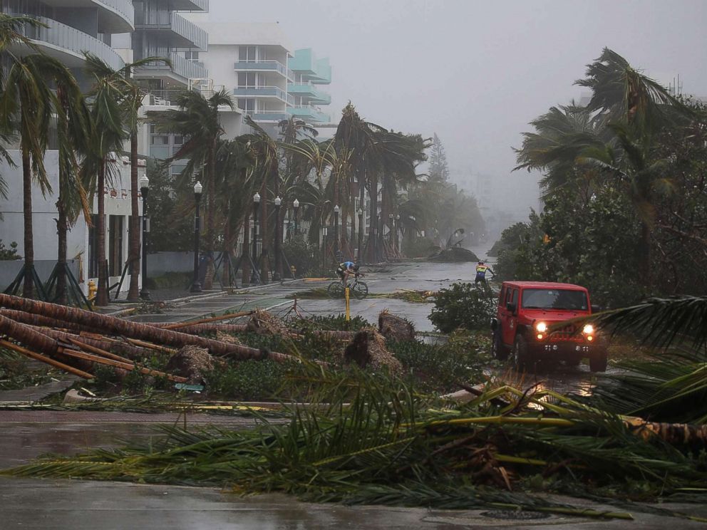 PHOTO: A vehicle passes downed palm trees and two cyclists attempt to ride as Hurricane Irma passes through the area on Sept. 10, 2017 in Miami Beach, Fla.