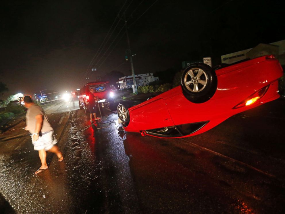 PHOTO: People tend to a car that flipped over on Cape Coral Parkway during Hurricane Irma, in Cape Coral, Fla., Sept. 10, 2017.