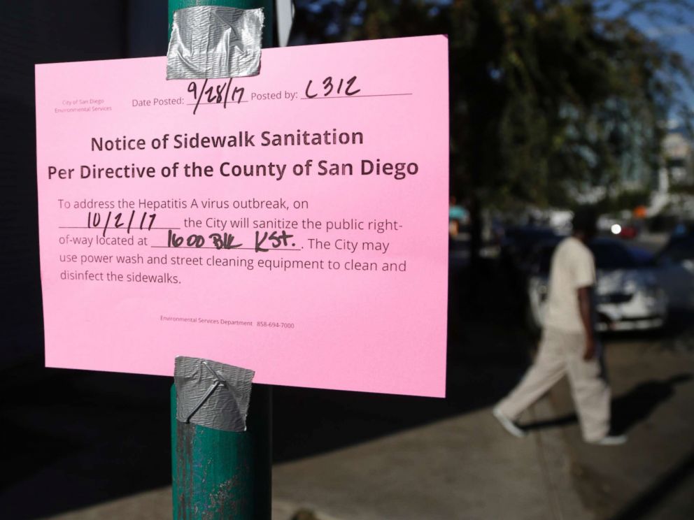 PHOTO: A man passes behind a sign warning of an upcoming street cleaning to address a hepatitis A outbreak in San Diego, Sept. 28, 2017.