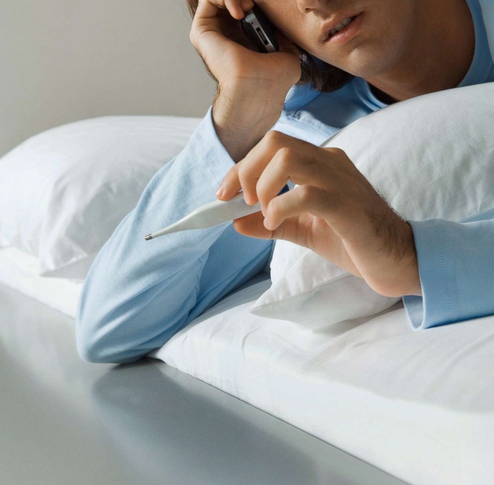 PHOTO: A man is pictured lying in bed, using a cell phone and holding up thermometer in this undated stock photo.