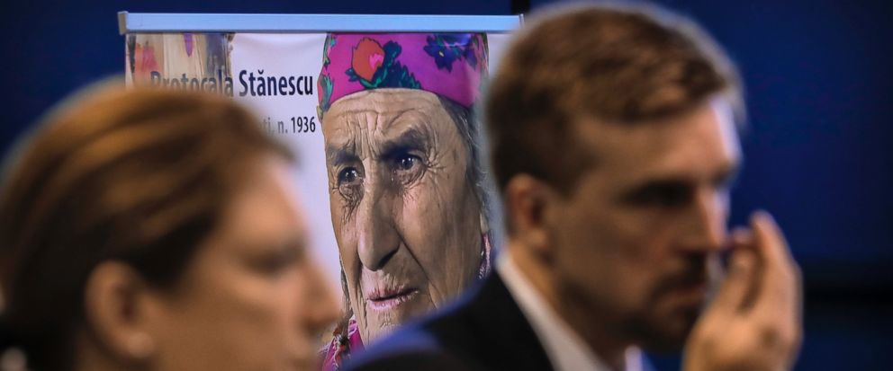 People attend a commemoration marking the extermination of thousands of Gypsies at a Nazi concentration camp, backdropped by the photograph of a survivor, in Bucharest, Romania, Wednesday, Aug. 2, 2017. Romanias foreign ministry said young generatio